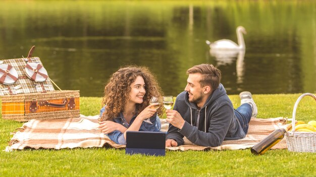 The couple lay on the grass and drink a wine on the river background