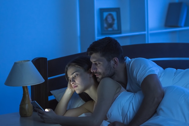 The couple lay with a phone in the bedroom. night time