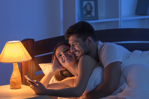 The couple lay with a phone in the bedroom. night time