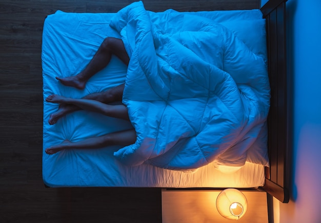 The couple laying under a duvet on the bed. evening night time, view from above