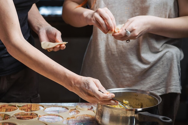 Couple of lesbian women are engaged in cooking dumplings in kitchen Unrecognizable female hands sculpt dumplings