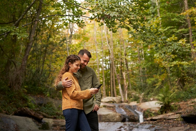 Couple looking at the mobil phone beside the river in the forest