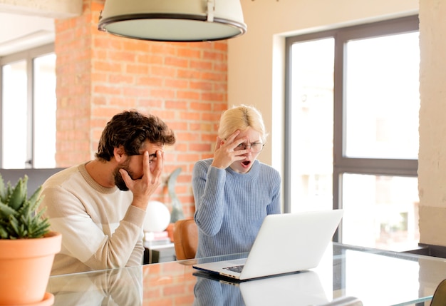 Photo couple looking shocked, scared or terrified, covering face with hand and peeking between fingers