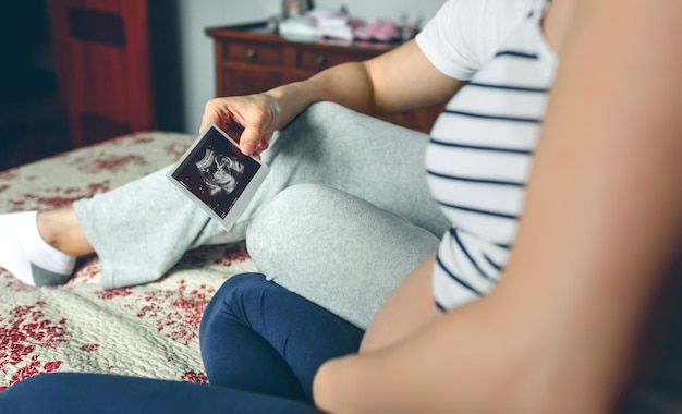 침대에 앉아 있는 아기의 초음파를 보고 있는 부부