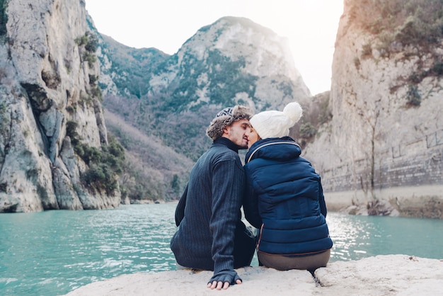 愛のカップルは、冬の山の風景の前でキスしています。愛、旅行、人々、ライフスタイルについての概念