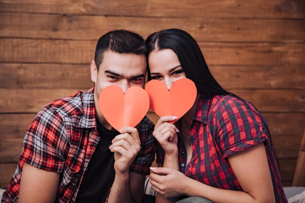 couple in love close their faces with paper hearts on Valentine's Day. Idea for a photoshoot for lovers