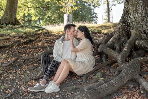 A couple in love, a couple and a girl sit under a beautiful tree and caress each other, kiss