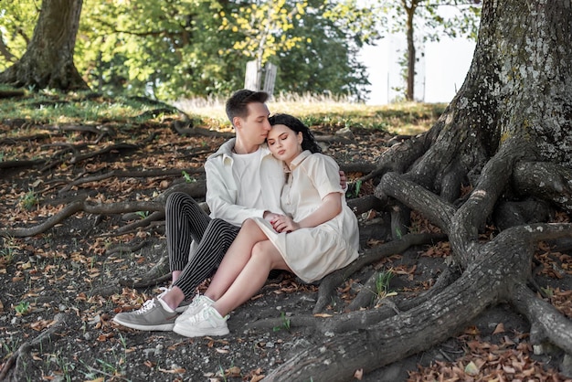 A couple in love, a couple and a girl sit under a beautiful tree and caress each other, kiss