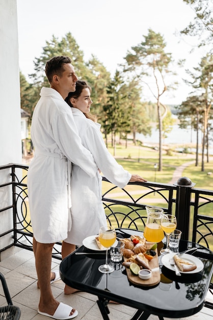 A couple in love cuddling on a hotel balcony in their bathrobes with breakfast on the table