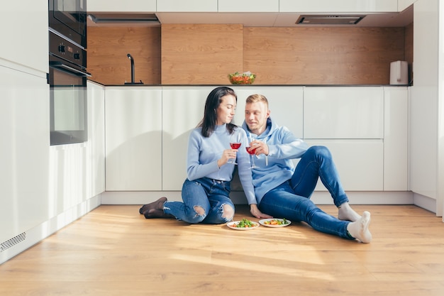 Coppia innamorata mangia un'insalata di verdure, seduto per terra in cucina e beve vino