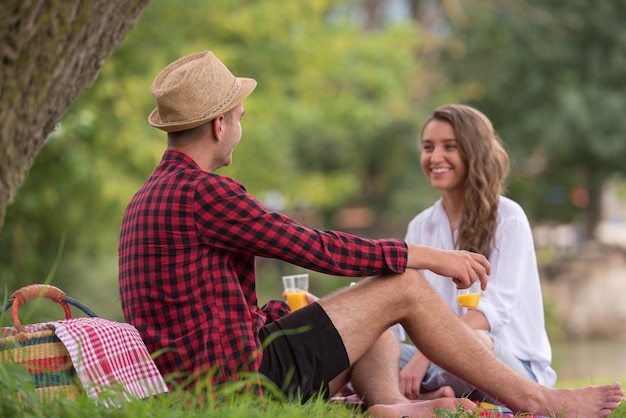 Влюбленная пара наслаждается напитками и едой во время пикника на красивой природе на берегу реки