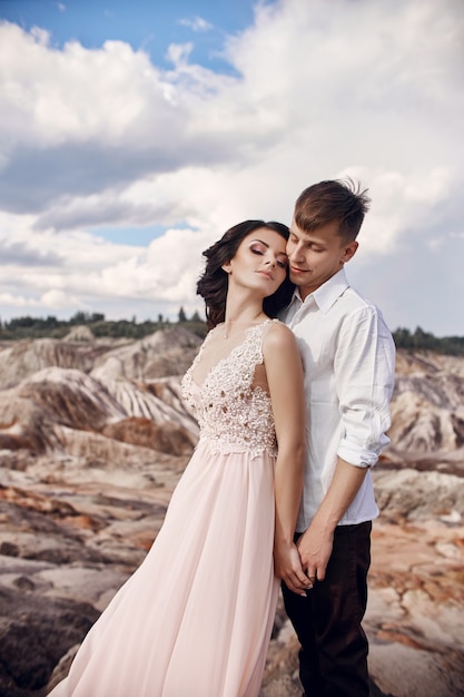 Couple in love in fabulous mountains hugging, Martian landscape. Lovers walk in the mountains in the summer, the girl in long light summer dress with a bouquet of flowers and a wreath on her head