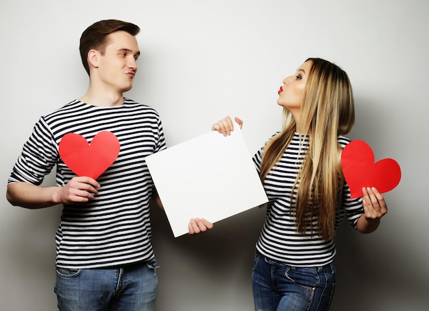 Couple, love and family concept: happy couple holding white blank and red hearts.