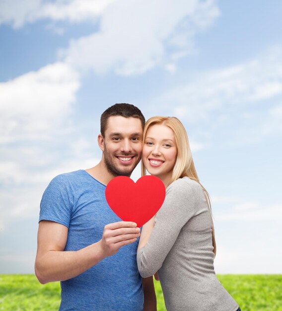 Concetto di coppia, amore e famiglia - coppia sorridente che tiene grande cuore rosso