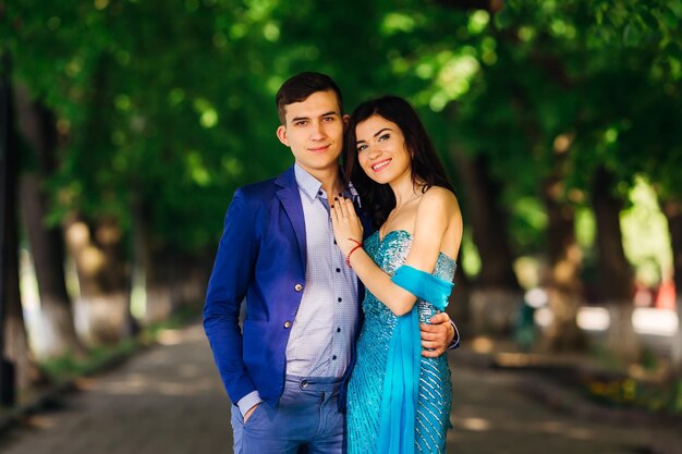 The couple in love in festive clothes look at the camera lens and smile in the park