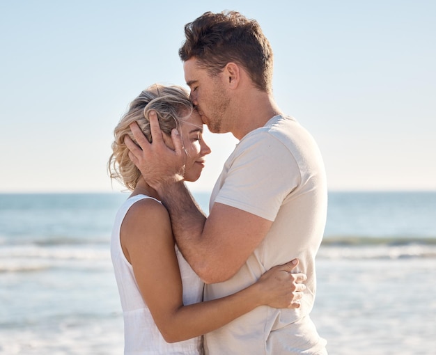 Couple love and forehead kiss on beach by ocean sea or Hawaii water waves in trust love and security Smile happy or bonding woman and man on anniversary summer break in tropical nature location