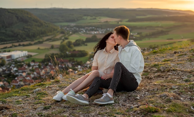 恋をしているカップル、男と女が夕日のキスとハグで山に座っている