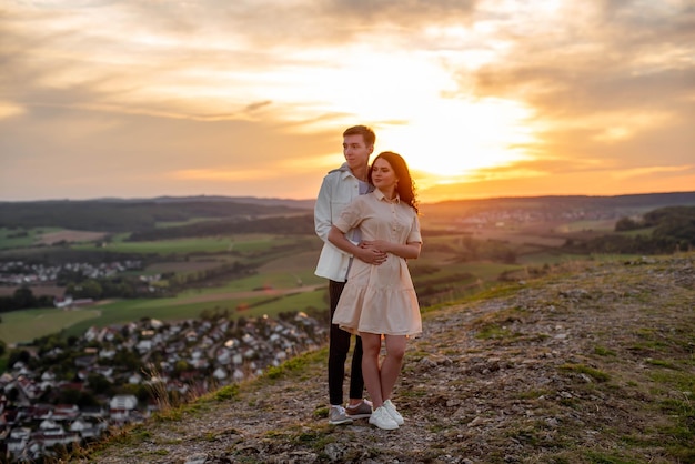 A couple in love, a guy and a girl are standing on a mountain at sunset hugging and kissing