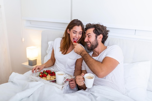 Coppia innamorata che fa colazione a letto. giovani coppie caucasiche che fanno colazione romantica a letto. femmina e maschio, due tazzine di caffè, frutta e biscotti colorati.