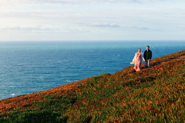 The couple in love hold hands and walk along the path on the shore of the ocean