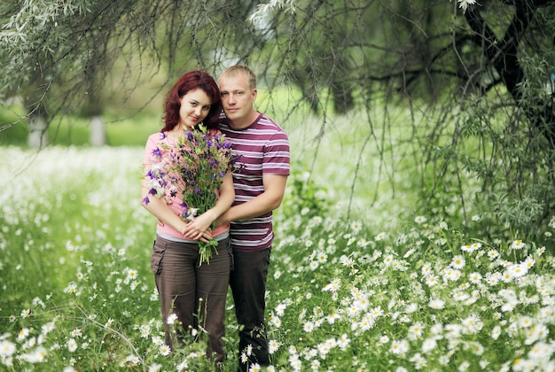 Couple in love holding a bouquet of flowers in a field of white daisies and green grass