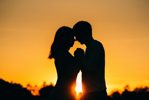 Couple in love holds hands at an orange sunset in summer