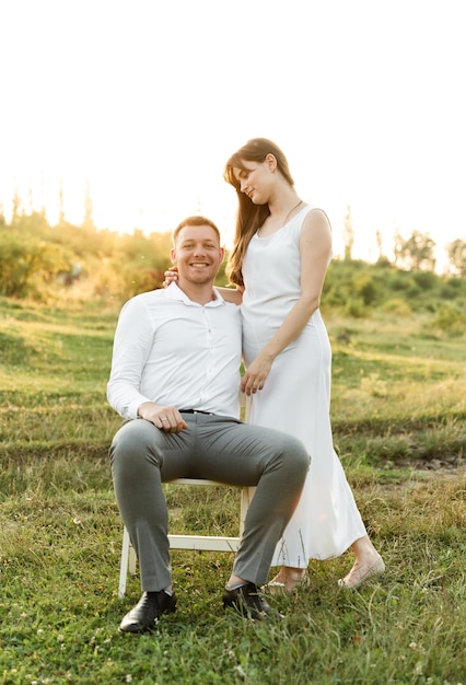 Couple in love hug and have fun at sunset on a sunny day. the guy sits on a chair and keeps his wife on his knees. family walk