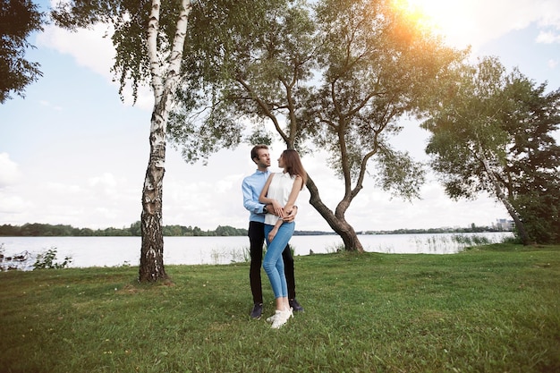湖の近くの芝生の上に立って愛の抱擁のカップル