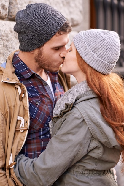 couple love and kiss with closeup in outdoor in against wall on cold weather together and support in london affection relationship and bonding for romance with soulmate care and happiness