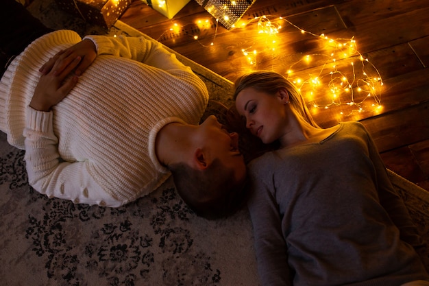 Влюбленная пара возле рождественской гирлянды лежит на полу дома