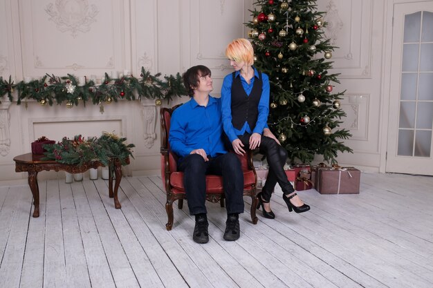 Couple in love sitting on sofa at home on Christmas tree on background