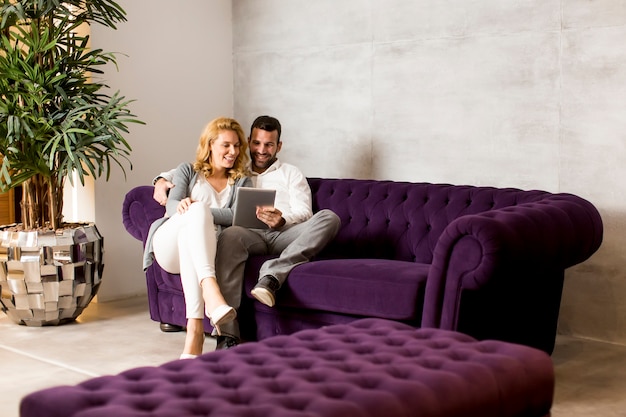 Photo couple in love sitting on sofa and watching something at tablet