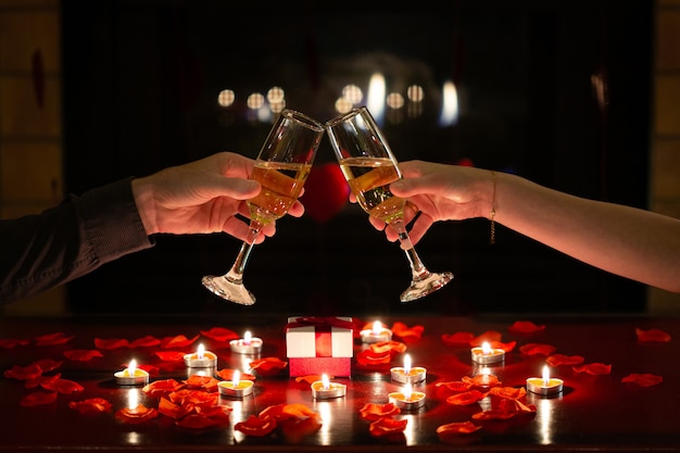 Couple in love toasting together with glasses of champagne to celebrate Valentines Day during romantic dinner Red roses gifts and flowers 