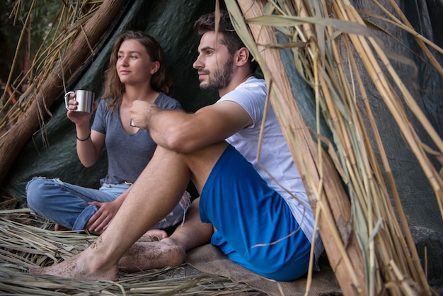 couple in love traveling and spending time together in straw tent while drinking hot tea by the river