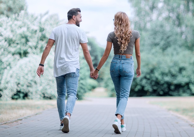 Photo couple in love walking in park holding handsrear view