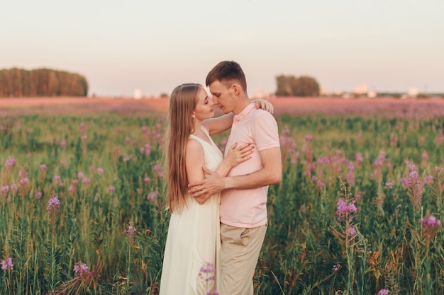 愛するカップルが花の牧草地を歩きます。愛と春が咲きます。男性は女性を抱きしめる