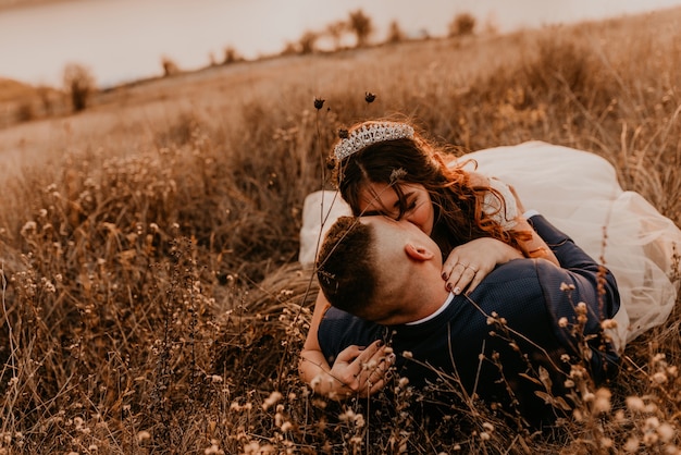 Coppia in amore matrimonio sposi novelli in abito bianco e vestito stanno camminando sdraiato campo di erba lunga in estate