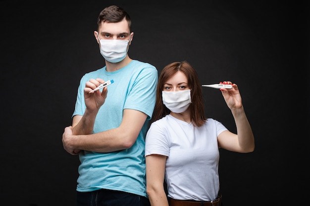 Couple in love in white medical masks are scared by coronavirus and shows thermometers