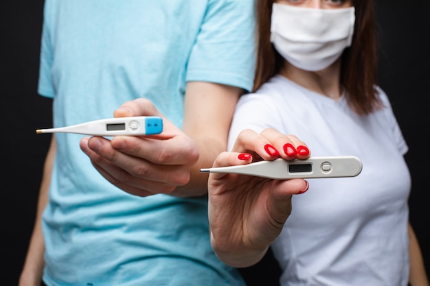 Couple in love in white medical masks are scared by coronavirus and shows thermometers