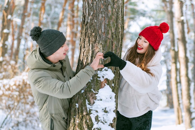 Couple in love in winter forest keeps hands in heart shape sign