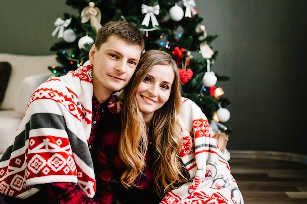 Couple in love with blanket sitting next to a Christmas tree.