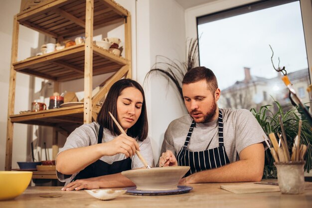 Photo couple in love working together on potter wheel in craft studio workshop