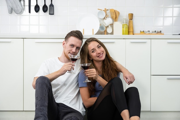 Couple lover sitting on kitchen floor and holding glasses of cocktail and enjoy drinking at home