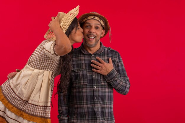 Couple of lovers with typical costumes of festa junina in studio photos on red background Brazilian June Festival