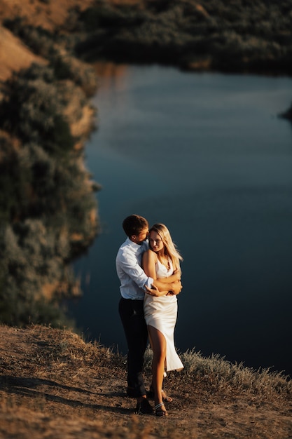 Couple of loving each other outdoors on a hill with lake . A couple of lovers are standing and hugging.