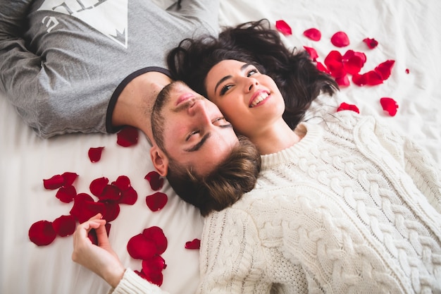 ヘッドとベッドの頭の上に横たわっているカップルは、バラの花びらに囲まれて