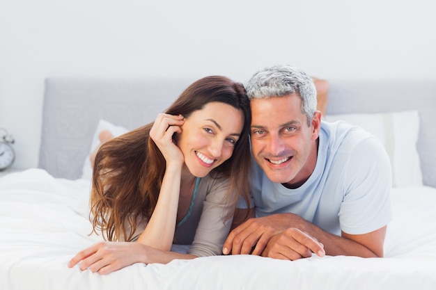 Couple lying on bed and smiling at camera 