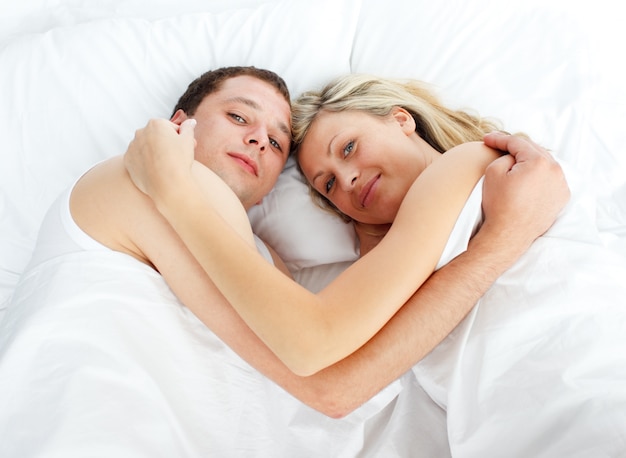 Couple lying in bed and smiling at the camera