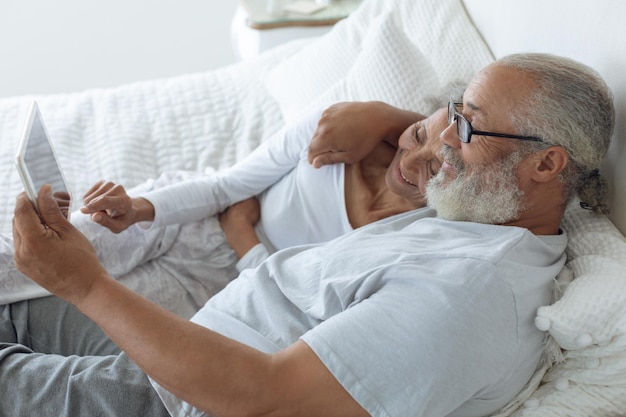 couple lying in bed and watching digital tablet
