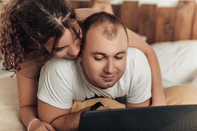 Photo couple lying on bed with laptop at home and hugging